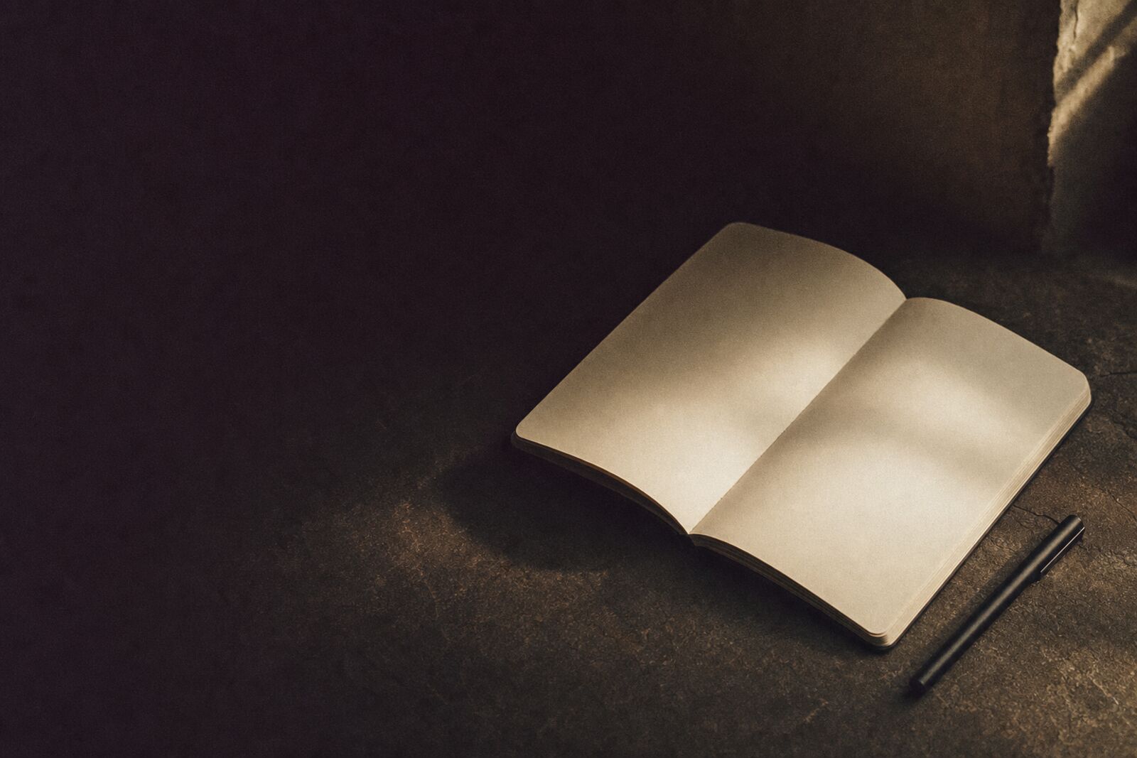 An open notebook and pen on a dark stone surface in warm gold light.